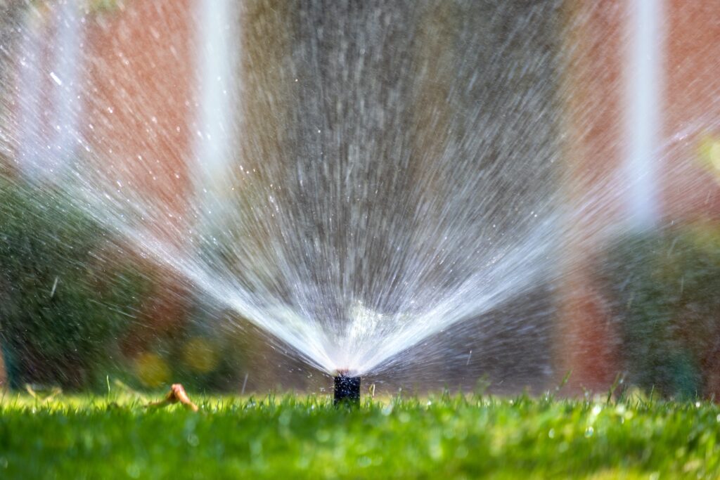 Plastic sprinkler irrigating grass lawn with water in summer garden. Watering green vegetation